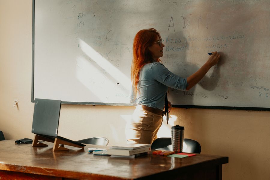 Docent schrijft op het whiteboard in een lokaal met daglicht